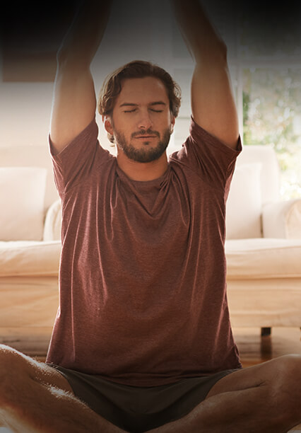 Bağdaş kurup oturan kişi, kollarını yukarı uzatarak sakin bir ortamda meditasyon yapıyor